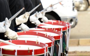 Four drums being played by white-gloved members of a drum corps.