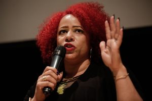 Nicole Hannah-Jones with her signature red hair style, left hand raised and right holding a microphone.