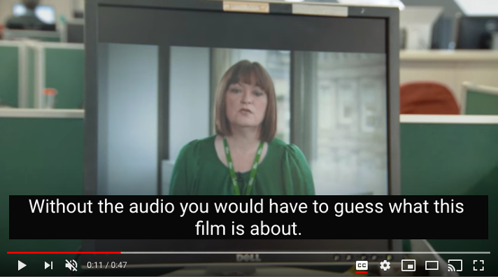 A screenshot of a youtube video showing a woman in a green shirt speaking. A black box with text on the video says, "Without the audio you would have to guess what this film is about".