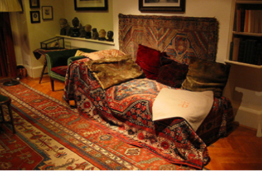 This photograph shows what Freud’s famous psychoanalytic couch looked like. The couch is draped in tapestries and pillows, and the room is decorated with sculptures, books and pictures on the wall.