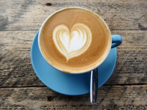 Image of a blue cup of coffee with a heart shape made with cream on top