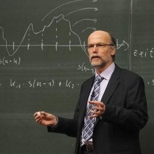 Man standing in front of a chalkboard talking.