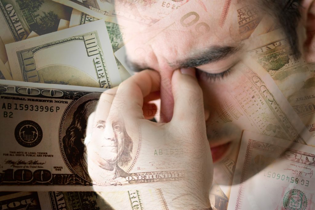 A young man exhibiting stress with money in the background.