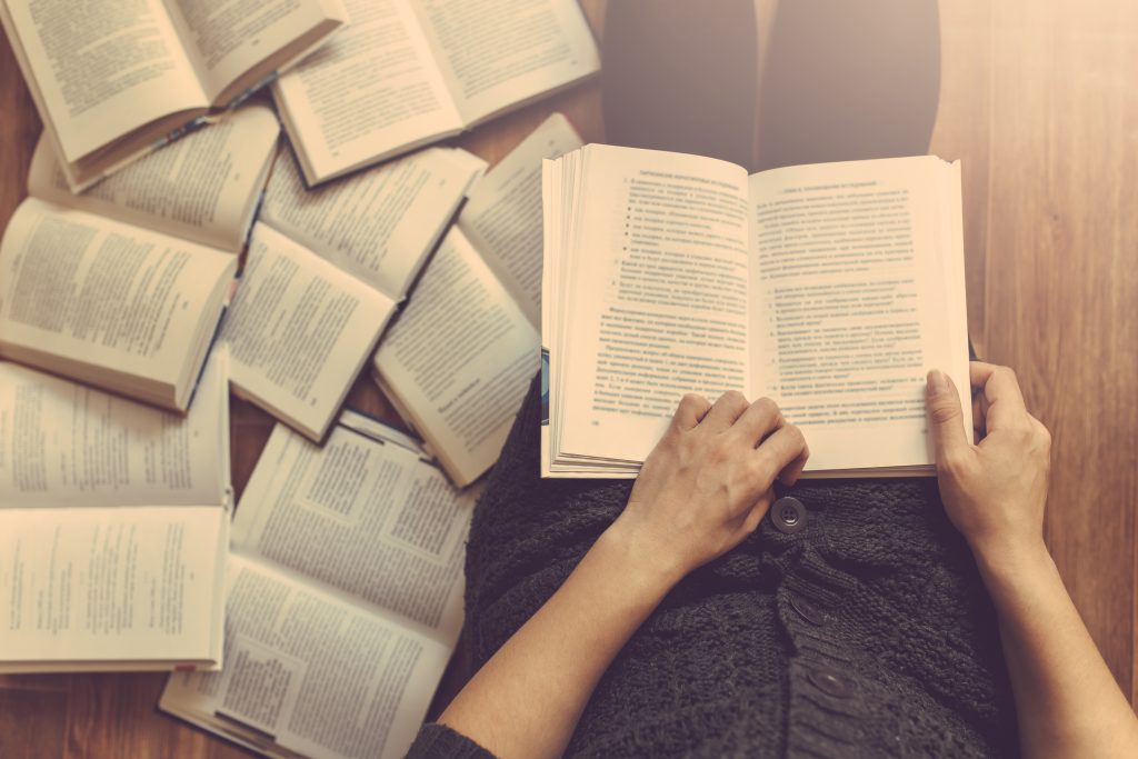 Person sitting on the floor surrounded by several open books.