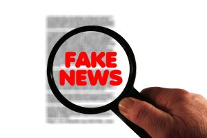Image of blurred text with a magnifying glass with fake news written in it.
