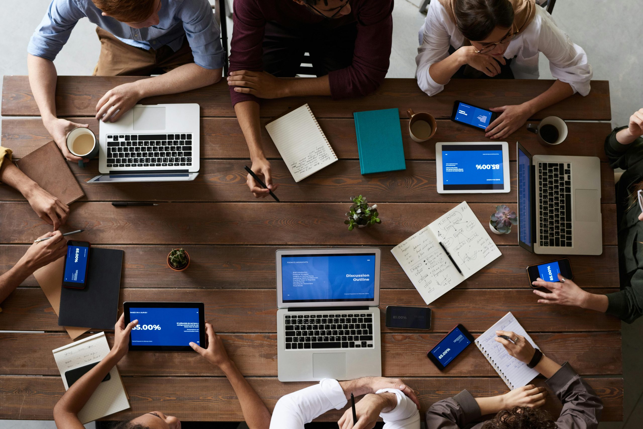 An overheard image of many people and their papers, computers and phones working at a table together.