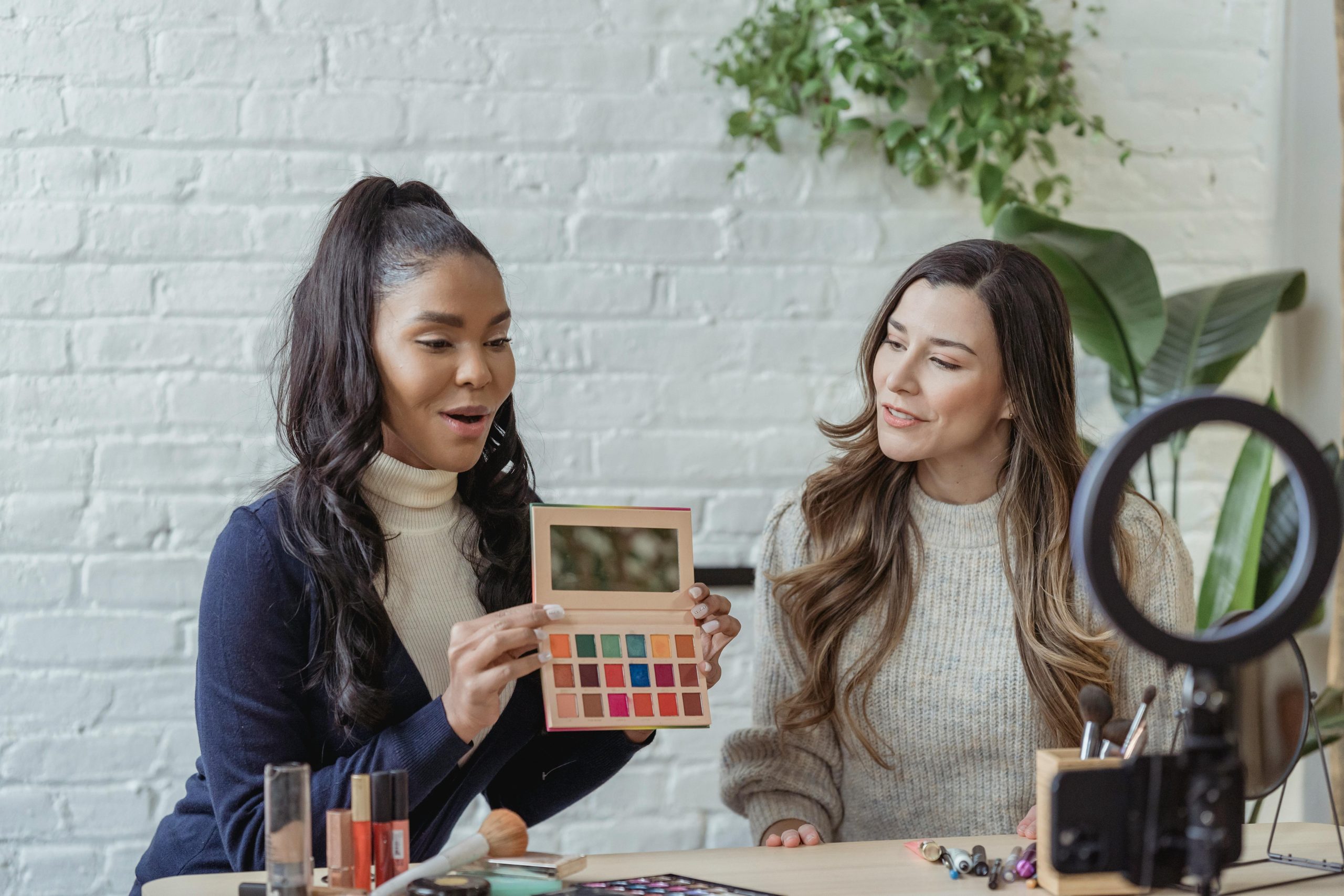 Young diverse ladies recording a video about makeup products on a smartphone.