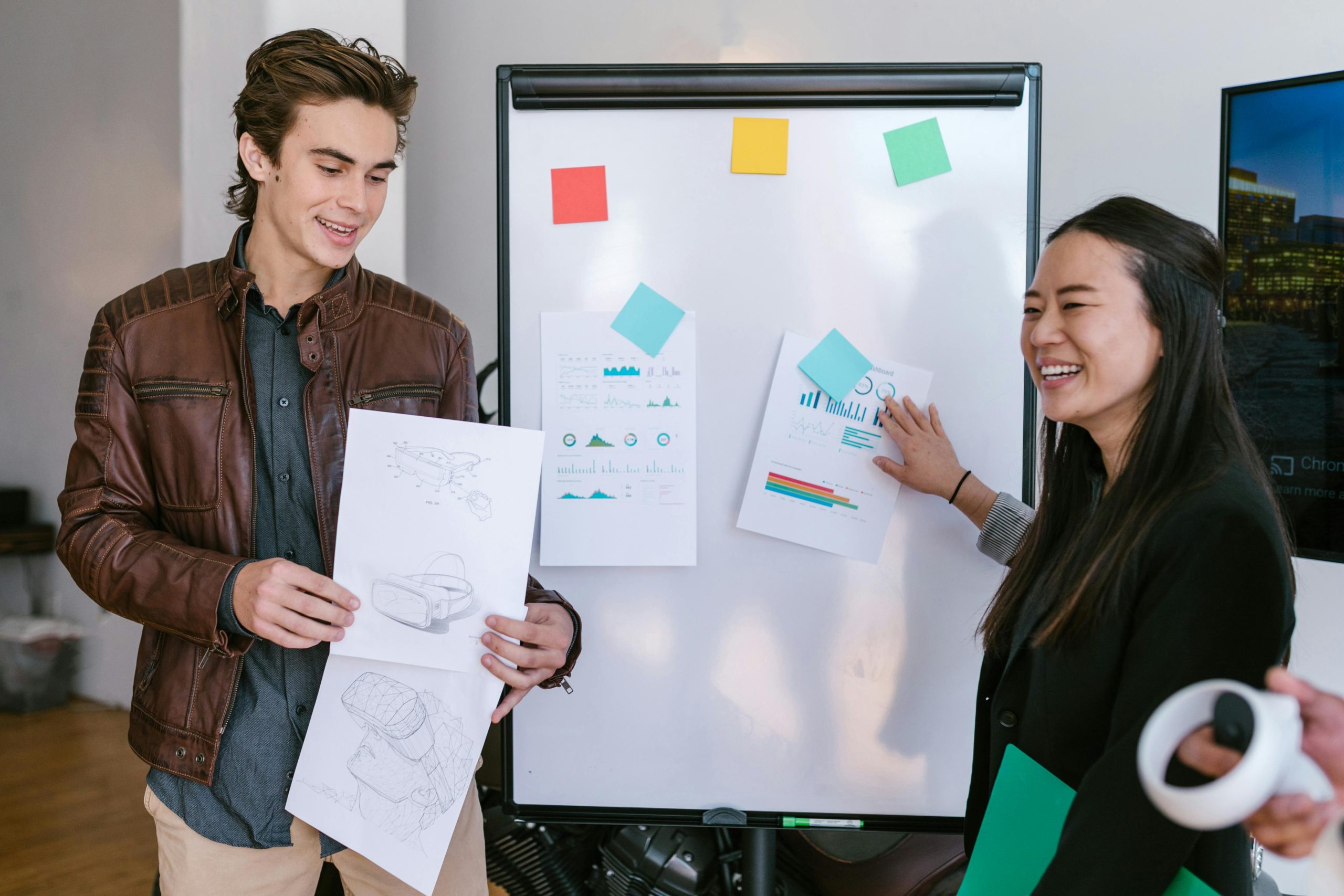 A photo of a man and women with notes on a whiteboard pitching ideas to people.