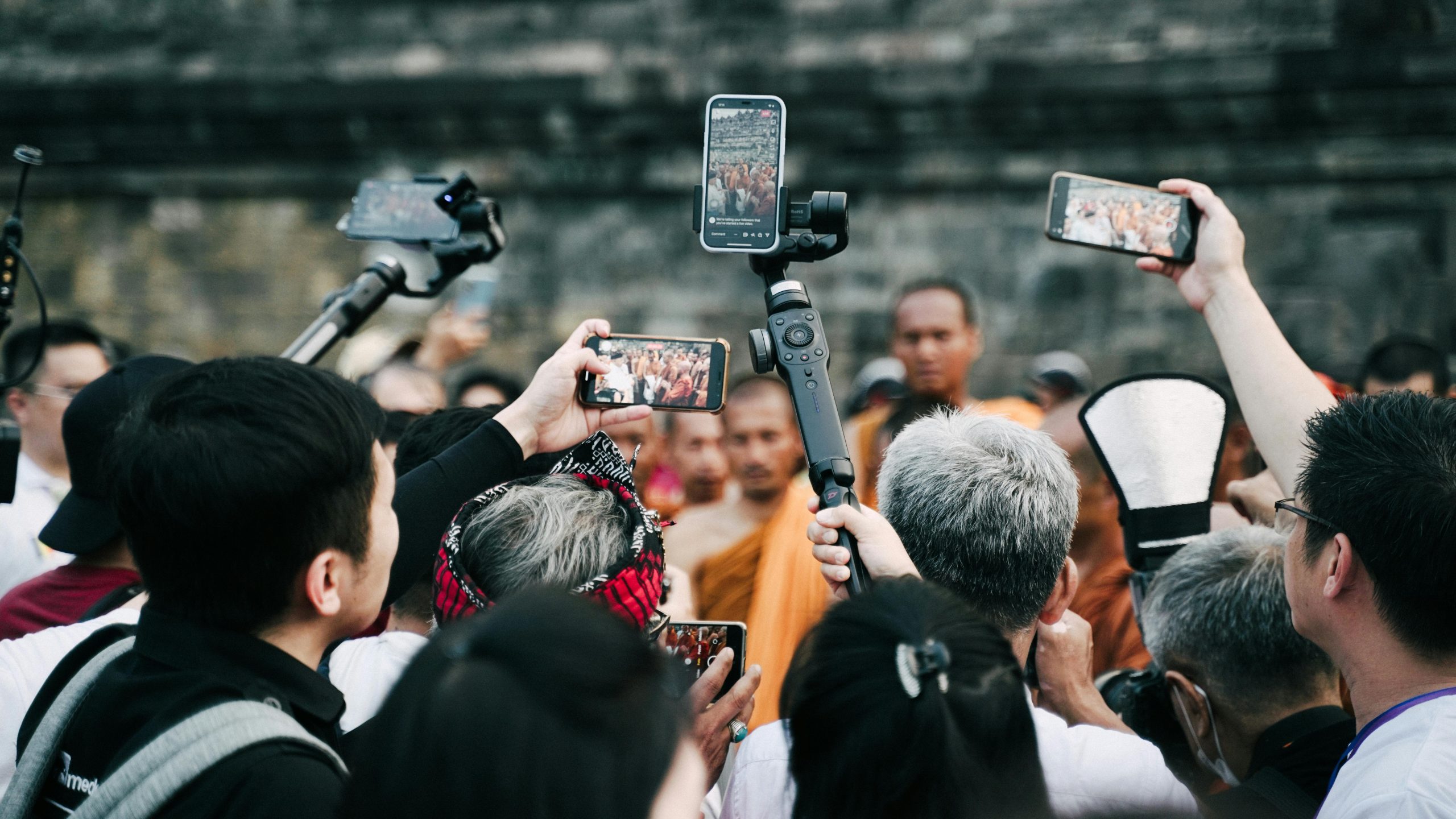 A swarm of people and their phone and cameras surround a source of media attention.