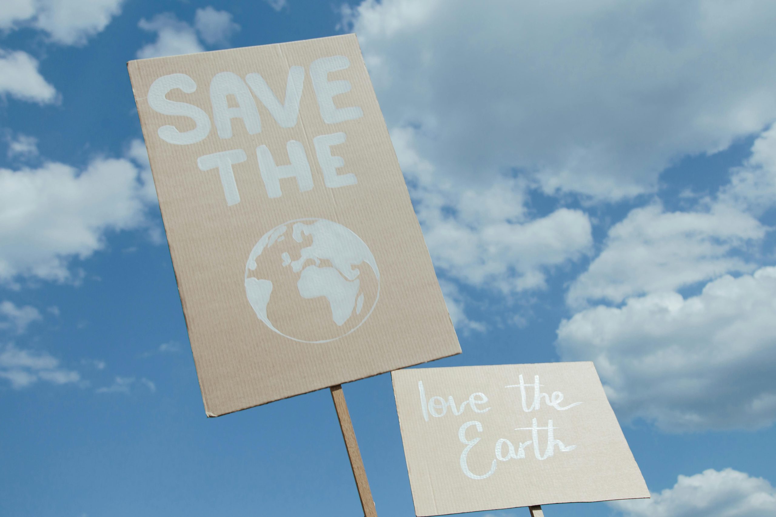 Two cardboard signs held against a blue sky spotted with white clouds say "love the Earth" and "save the Earth."