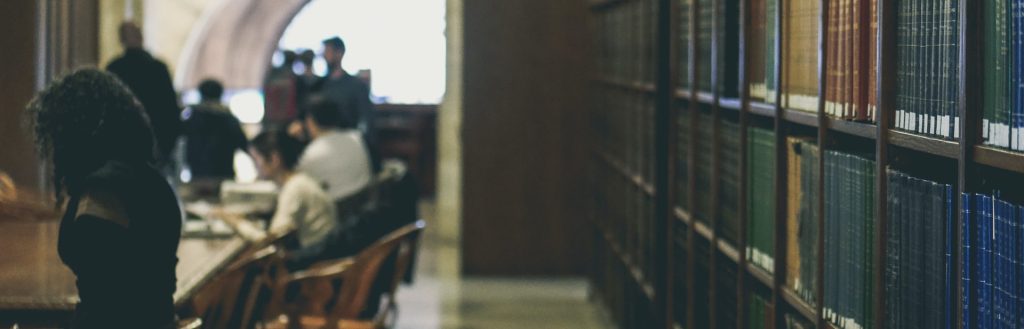 Students walking and studying at tables in a college library, with books