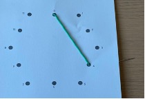 A sheet of paper with 12 dots arranged in the shape of a hexagon. A thick green string is threaded from the top center dot to the dot that is 4 dots away counterclockwise.