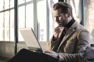 A handsome man looks at his laptop, confused