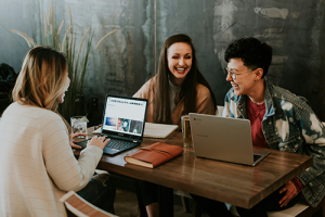 Three friends, smiling, sitting at a cafe table, laptops out