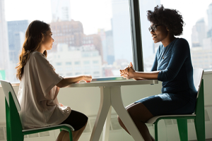 Two women sitting facing each other at a table and talking.