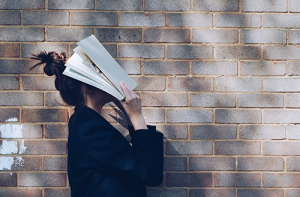 Woman holding book over her face in frustration