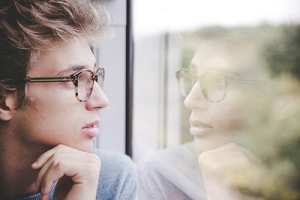 Man looking out a window, face reflected on the glass