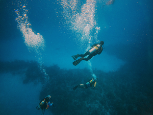 Three scuba divers underwater with bubbles streaming up from their masks