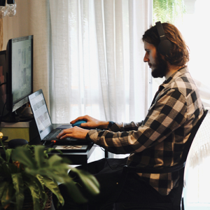 A man seated at a laptop, wearing headphones, hands on keyboard.