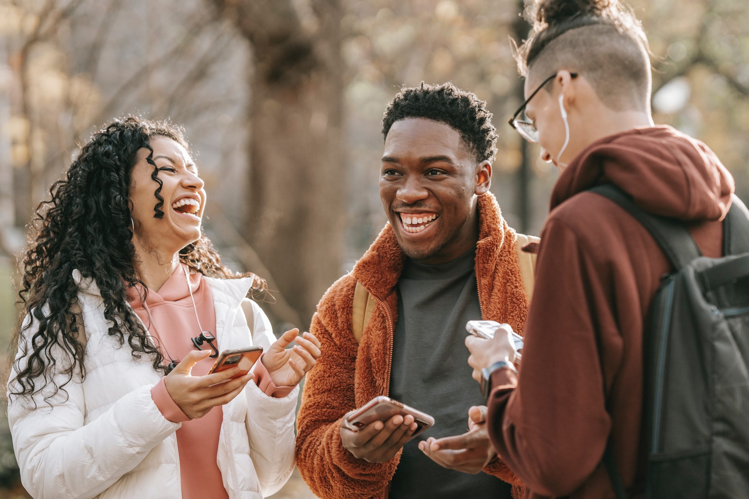 Three students stand outside looking at their cell phones and laughing.