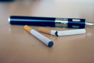 Photograph of a vape pen and cigarettes, one broken.