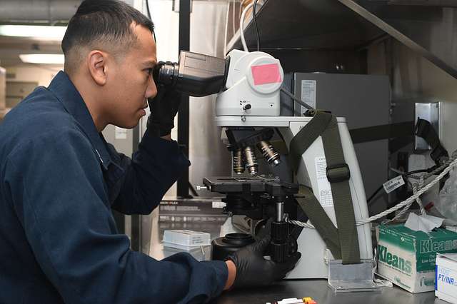 Photograph of a corpsman looking at a urine sample through a microscope onboard the USS Harry S Truman.