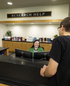 Librarian helping patron at research help desk.