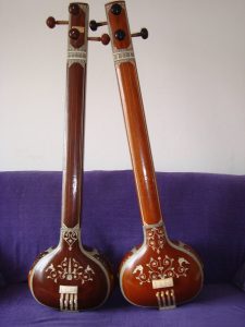 Two intricately decorated wooden tanpuras resting upright against a purple couch.