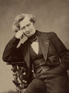 A sepia-toned photo of a man in a formal suit, sitting in an ornate chair with a contemplative expression.