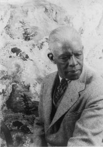 Portrait of an older man in a suit seated against a marble-patterned backdrop.