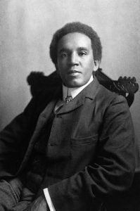 Black-and-white portrait of a man in a suit seated in a carved wooden chair.