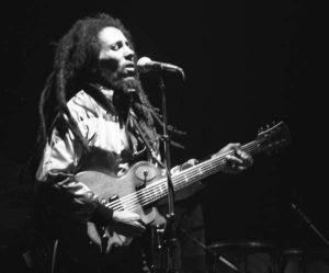 Musician playing guitar and singing on stage in a dark environment.