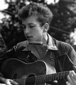 Person playing guitar and harmonica outdoors.