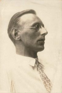 Sepia-toned profile portrait of a man wearing glasses and a patterned tie.