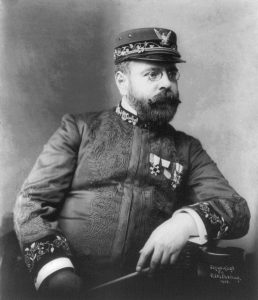 Black and white photo of John Philip Sousa in an embroidered military uniform with medals, wearing a cap and glasses.