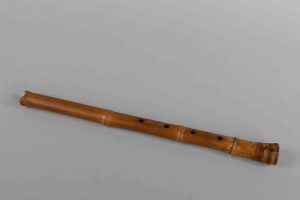 A traditional bamboo flute with five finger holes against a gray background.