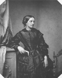 A black-and-white portrait of a woman in a 19th-century dress holding a book.