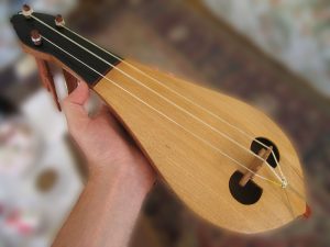 A person holds a small stringed instrument with a teardrop-shaped wooden body and four strings.