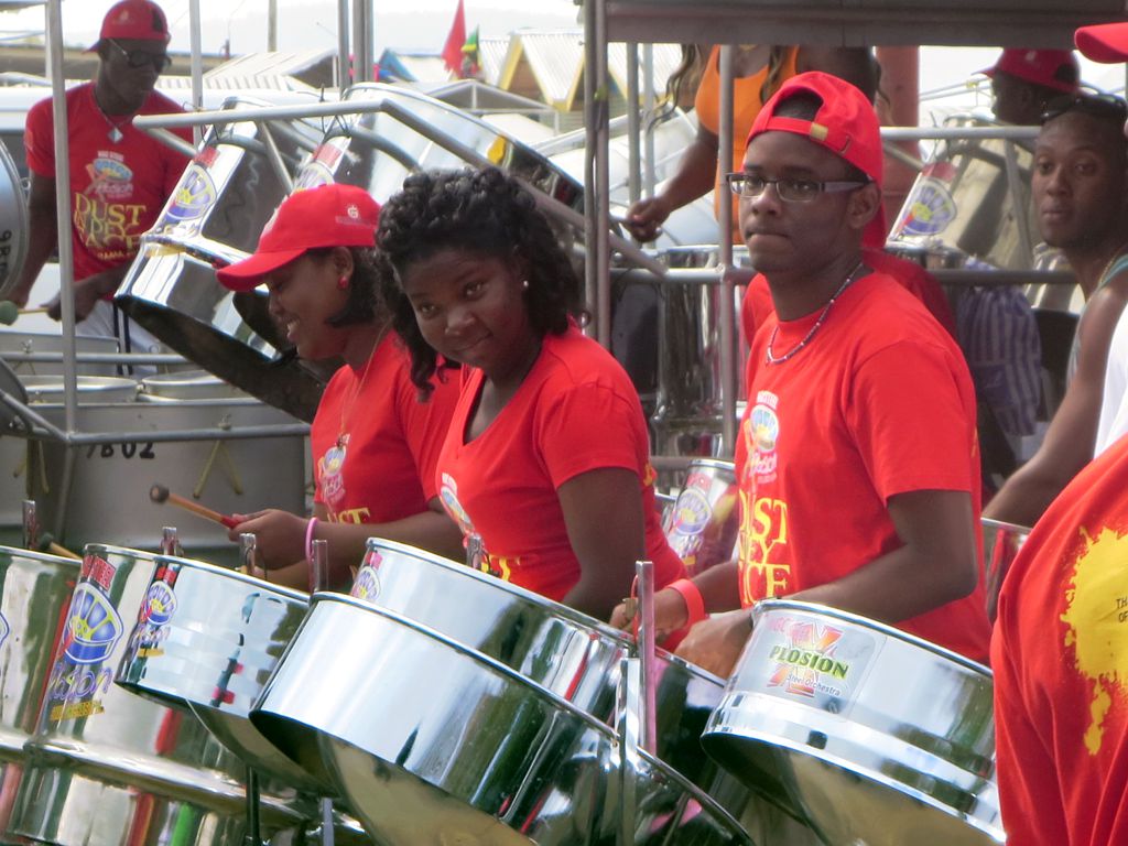 Musicians wearing red t-shirts and playing steel drums at an outdoor event.