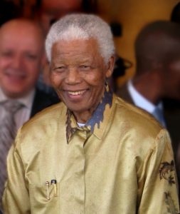 Photo of Nelson Mandela with white hair wearing a patterned gold shirt.