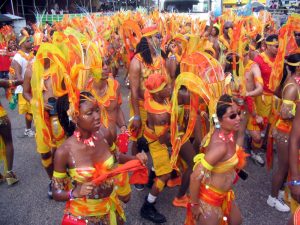 A group of people in colorful orange and yellow costumes dance in a parade.