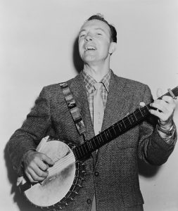 Person smiling and playing a banjo with a decorated strap.