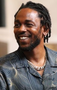 Person smiling while wearing a patterned shirt and a silver chain necklace.