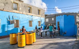 A group playing steel drums in a courtyard surrounded by blue-painted buildings.