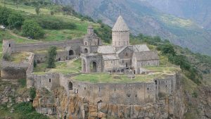 Ancient stone monastery on a cliff with a conical dome, surrounded by mountains.