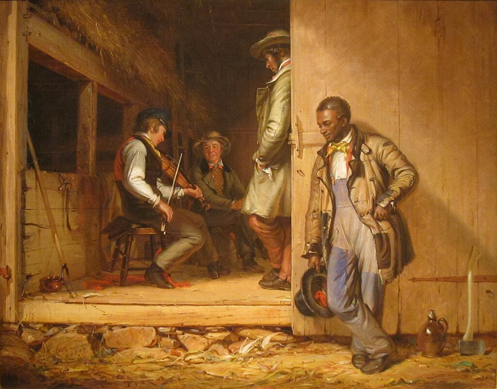 Three men gathered in a rustic wooden barn, with one playing a fiddle. A fourth man stands outside the door, listening.