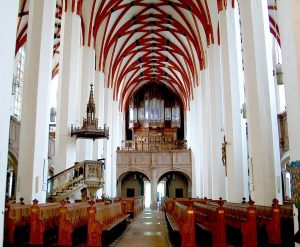 Interior of a gothic-style cathedral with red and white arched ceiling and wooden pews.
