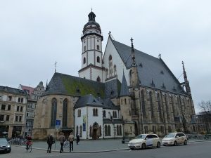 Large Gothic church with a central tower, surrounded by an urban setting with people and vehicles.