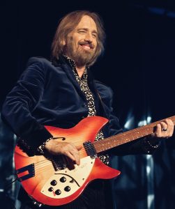 Musician in a blue velvet jacket playing an orange sunburst electric guitar.