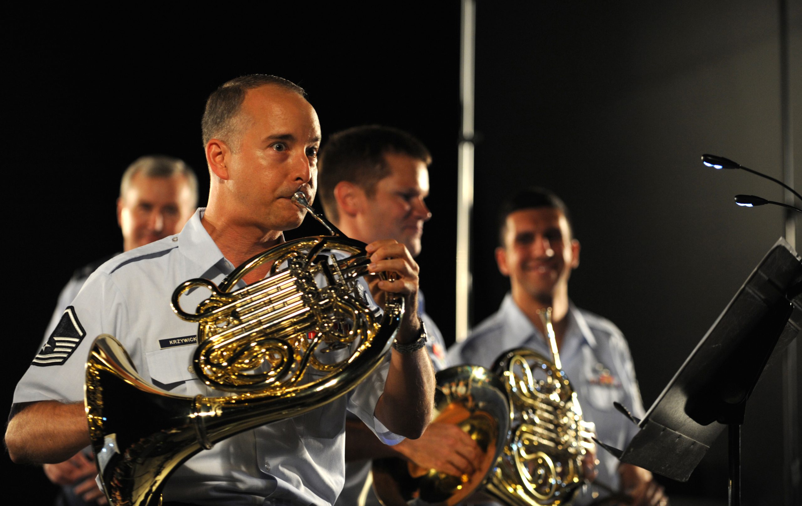 A group of musicians in uniform playing French horns.